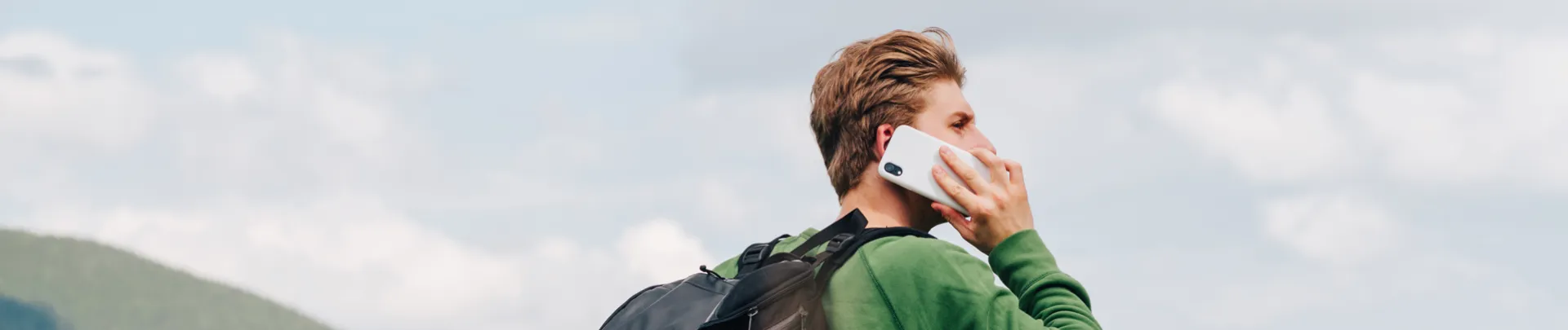 Een jonge mannelijke toerist belt in de bergen en kijkt weg.